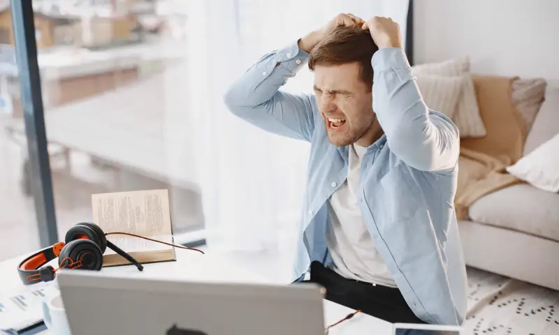 Homem sentado à mesa, com expressão de estresse, rodeado por ferramentas de trabalho, representando o impacto do estresse no cotidiano profissional.