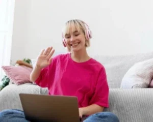 Mulher adulta sorrindo durante uma sessão de terapia online, sentada com um laptop e fones de ouvido.