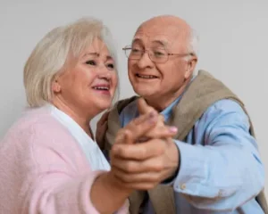 Casal idoso sorrindo e dançando juntos, simbolizando o bem-estar emocional e a conexão na terceira idade.